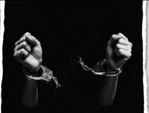 Black and white photo - stark black background. Hands handcuffed, breaking the handcuff chains between them.